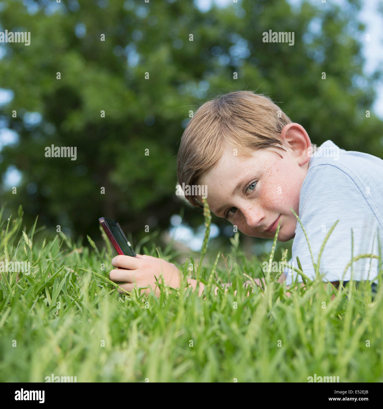 Ein kleiner Junge sitzt auf dem Rasen mit einer Hand gehalten elektronische Spiele Gerät. Stockfoto