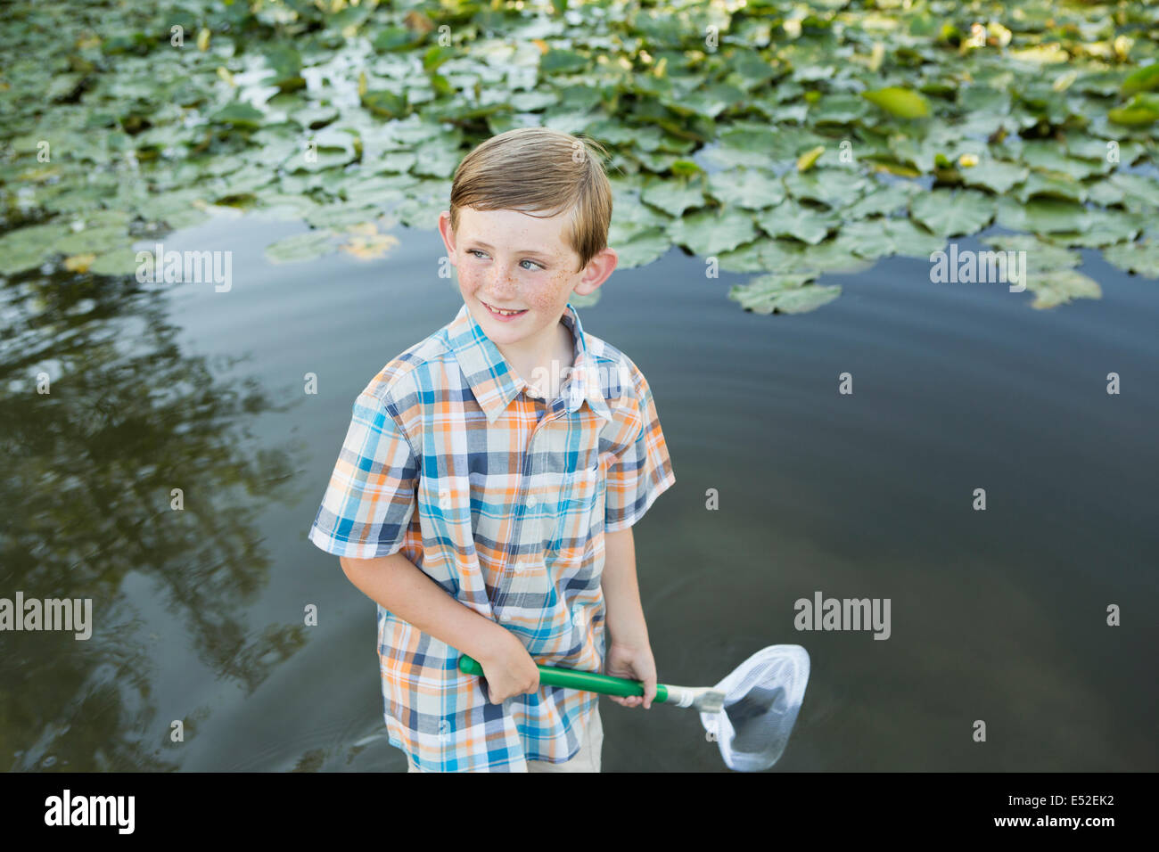 Ein kleiner Junge stehen im flachen Wasser mit einem Fischernetz. Stockfoto