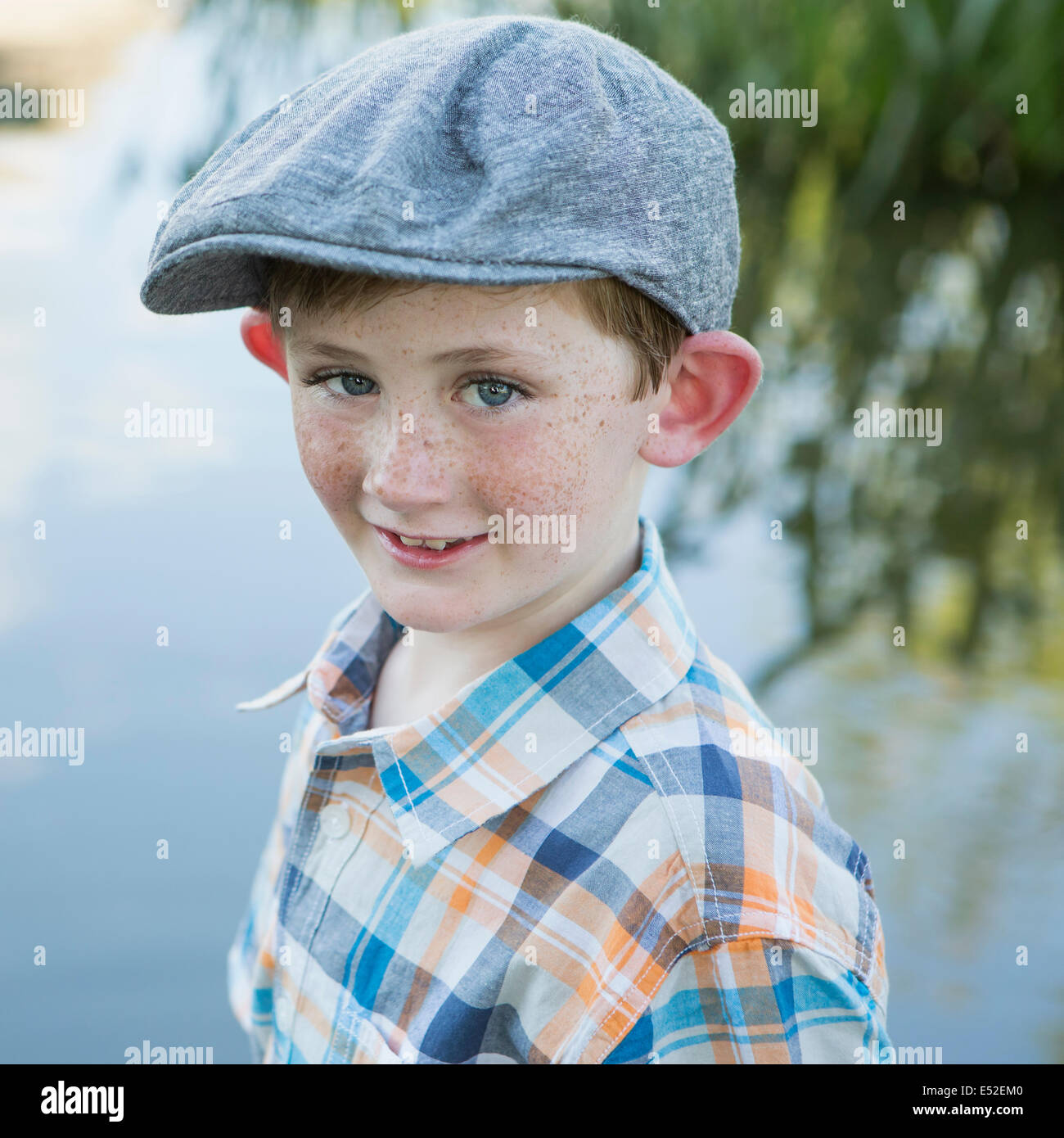 Ein kleiner Junge mit einem aufgegebenen Hemd und Tuch Mütze mit einem großen Rand stehen am Ufer eines Flusses. Stockfoto
