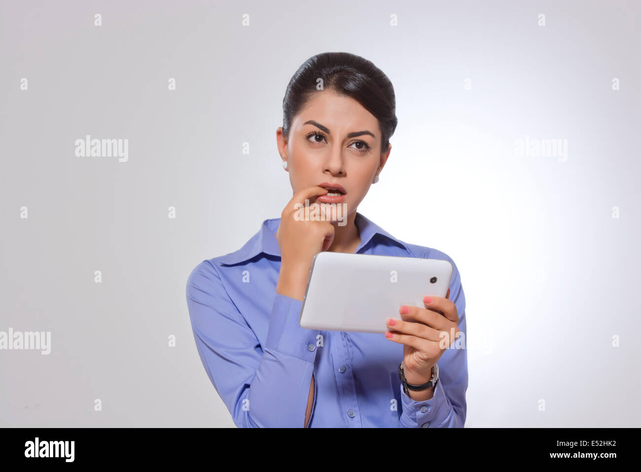 Nachdenklich Geschäftsfrau mit Finger im Mund hält digitale Tablet über grauen Hintergrund Stockfoto