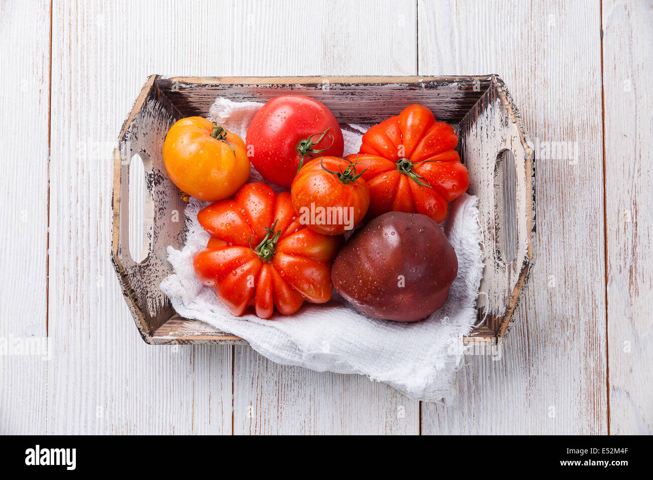 Reife frische bunte Tomaten in Holzkiste auf weißem Holz Hintergrund Stockfoto