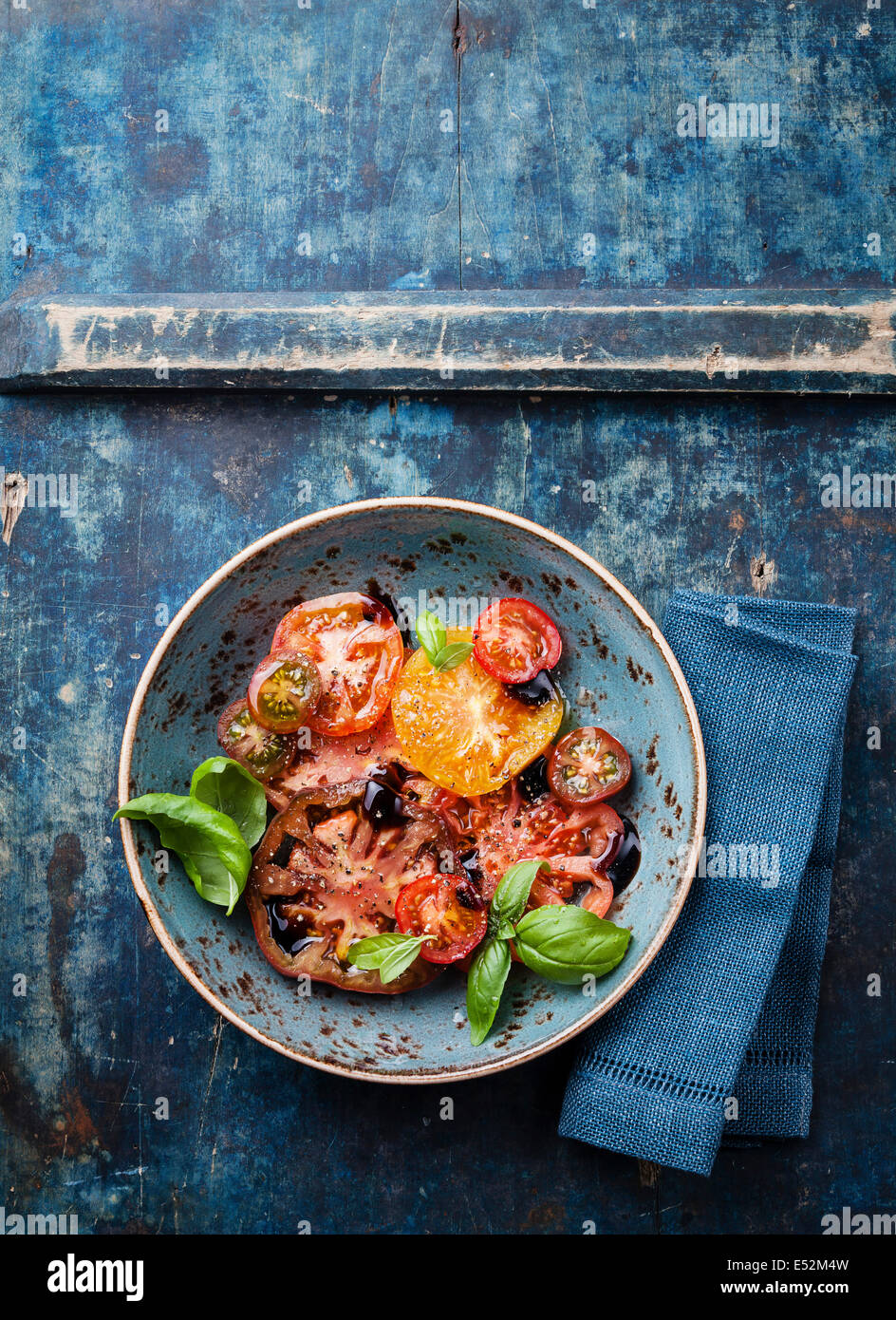 Reife frische bunte Tomaten Salat mit Olivenöl und Balsamico-Essig auf blauem Hintergrund aus Holz Stockfoto