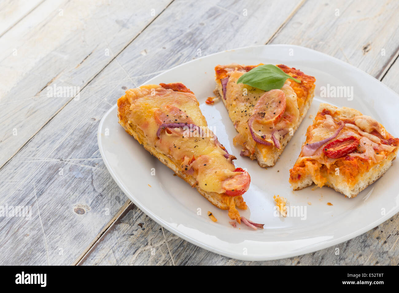 übrig gebliebene Pizza vom Vortag auf einer Platte auf einem rustikalen Holztisch Stockfoto