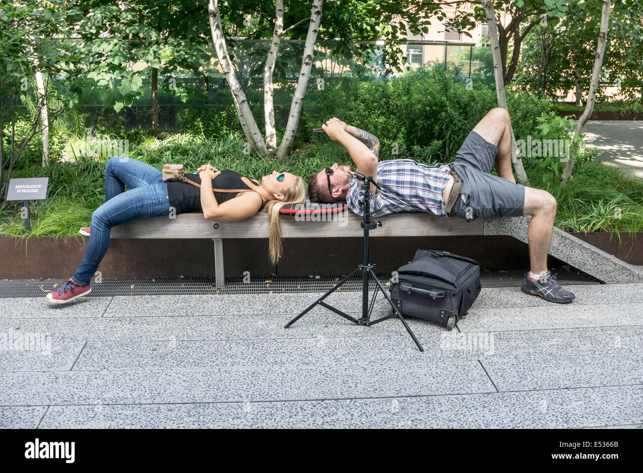 junge Touristen-paar eine Pause um ihre Fotos auf einer High Line Parkbank im Schatten von üppigen Sommer Laub Manhattan zu überprüfen Stockfoto