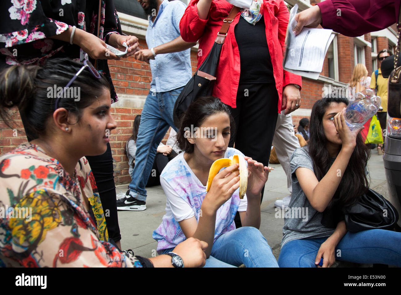 London, UK. Samstag, 19. Juli 2014. Pro-palästinensische Demonstranten in die Zehntausende marschieren durch die Londoner an die israelische Botschaft aus Protest gegen die militärische Offensive im Gazastreifen durch Israel. Mädchen, Ramadan, Fasten, ohnmächtig wird und mit Wasser und eine Banane von ihrer Familie wiederbelebt wird, wie sie Papier, um sie abkühlen winken. Bildnachweis: Michael Kemp/Alamy Live-Nachrichten Stockfoto