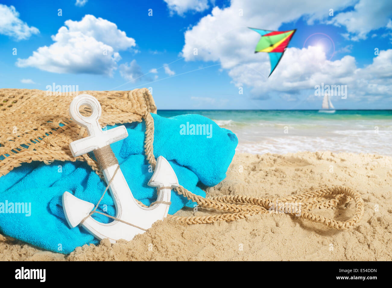 Strandtasche in den Sand mit Handtuch und Drachensteigen über dem Ozean Stockfoto