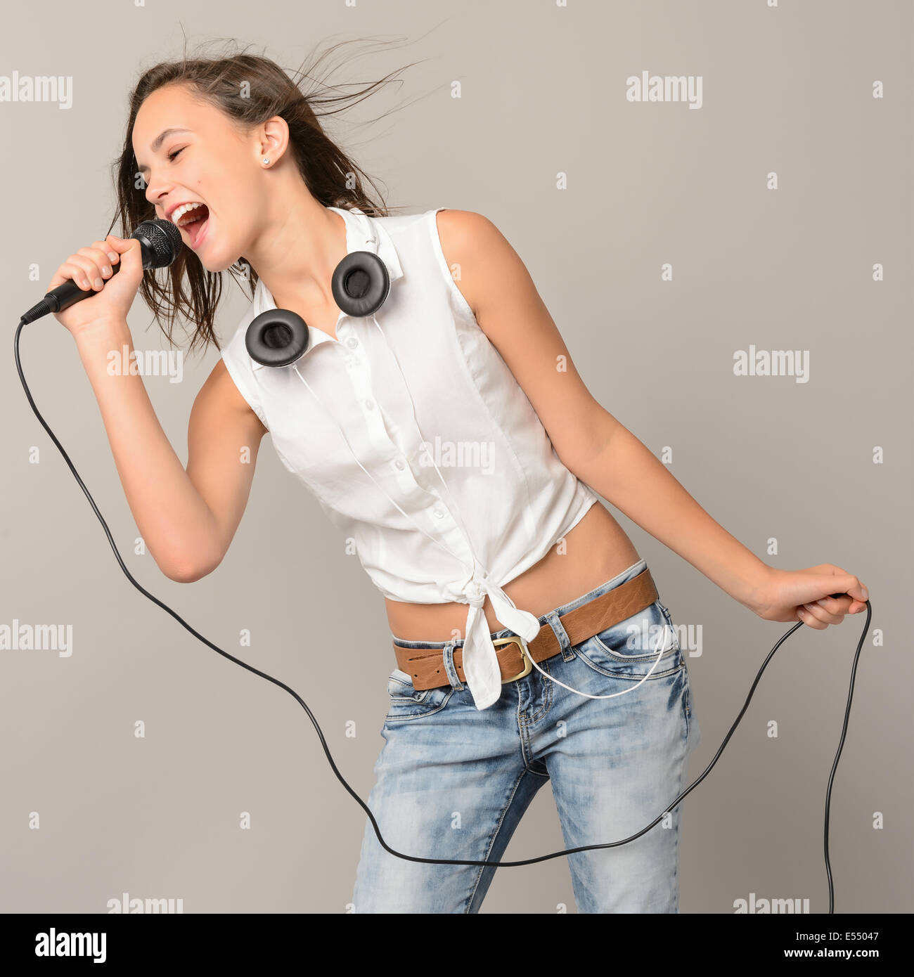 Teenager-Mädchen mit Mikrofon Karaoke Musik singen auf grauem Hintergrund Stockfoto