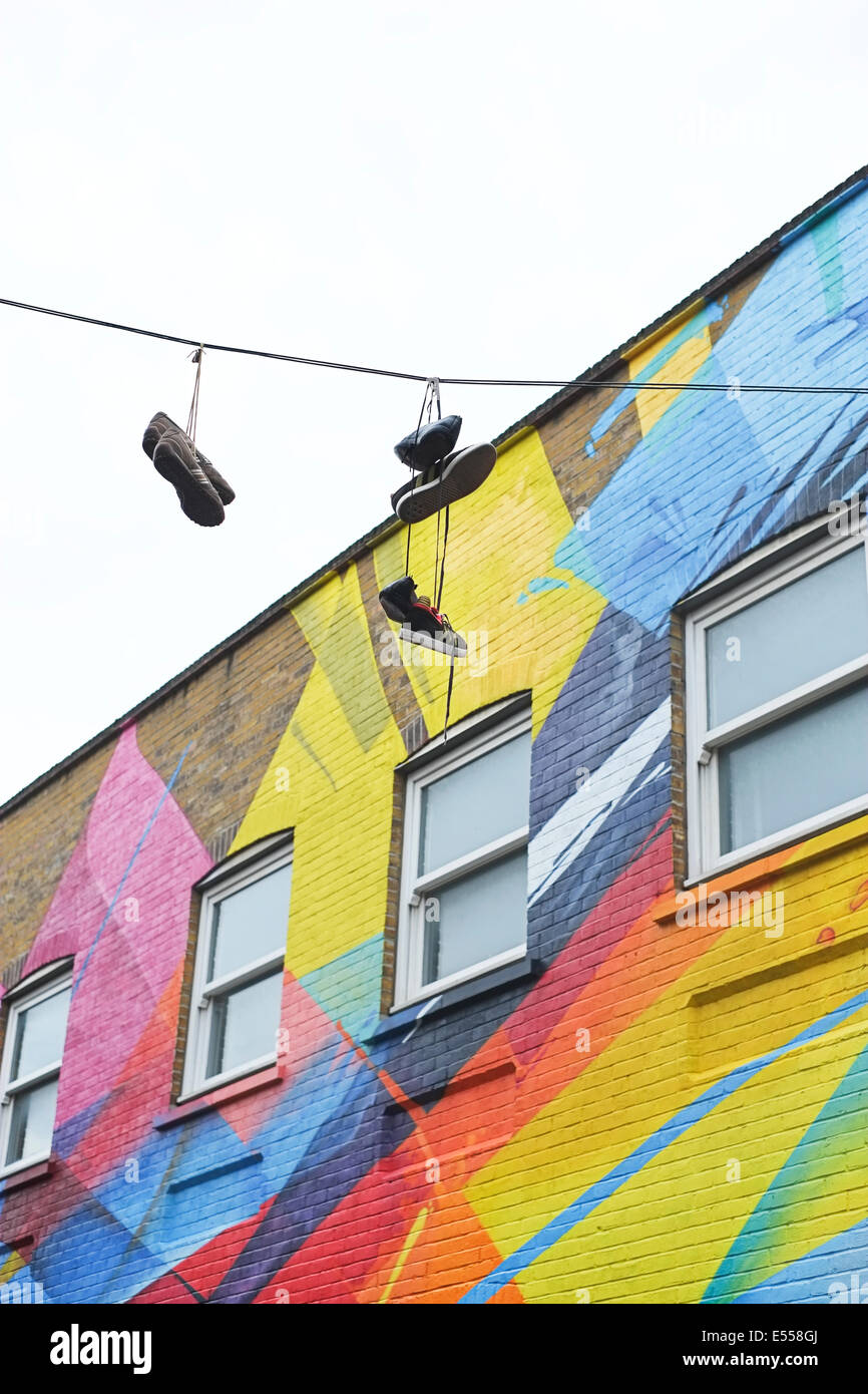 Schuhe hängen vom Kabel über Straße in Shoreditch, East London, England, UK, mit bunten Graffiti-Gebäude Stockfoto