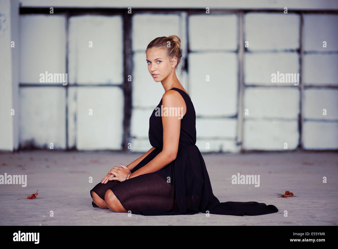 Junge Frau im schwarzen Kleid auf dem Boden kniend Stockfoto