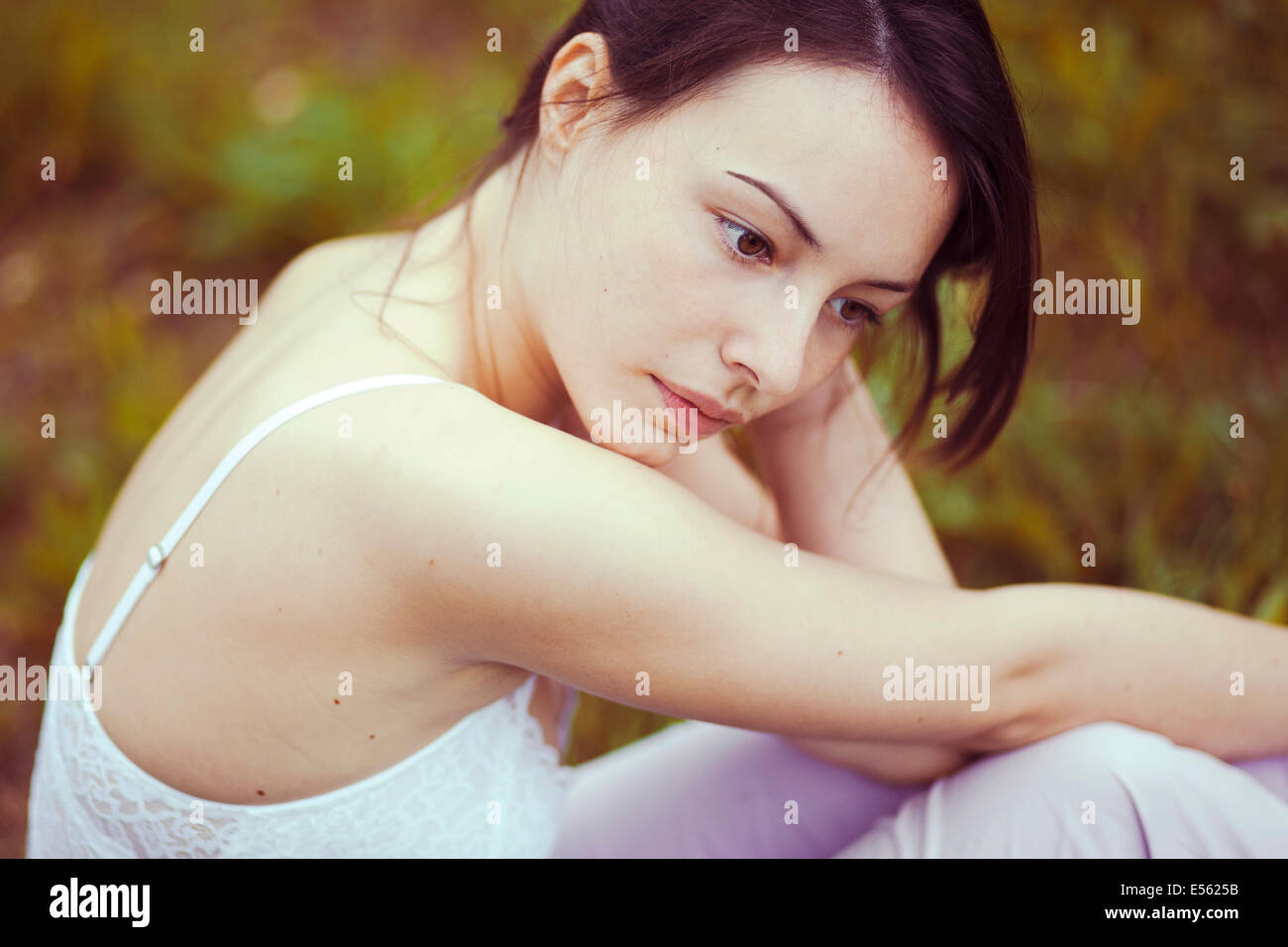 Junge nachdenkliche Frau sitzt auf einer Wiese Stockfoto