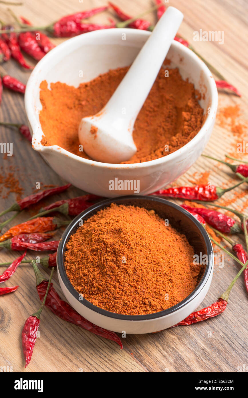 rote Paprika-Chili-Pulver in einem Mörser und Hülsen auf einem Holztisch Stockfoto