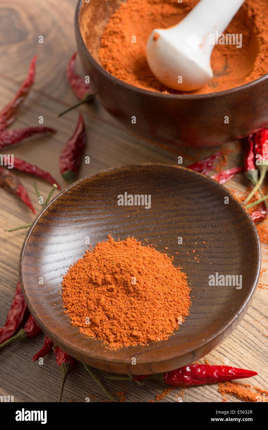 rote Paprika-Chili-Pulver in einem Mörser und Hülsen auf einem Holztisch Stockfoto