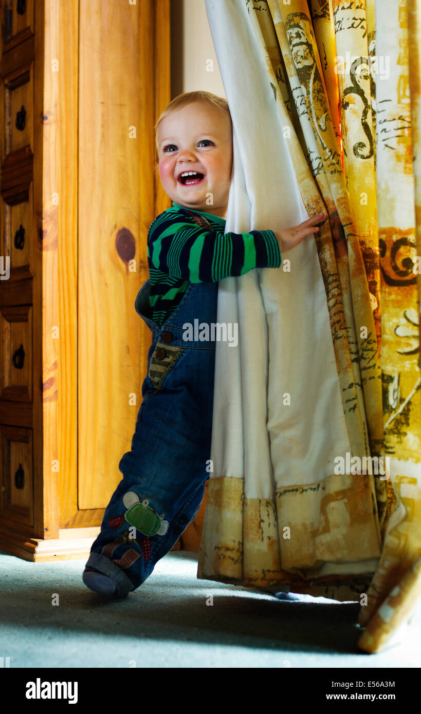 Ein fröhlicher kleiner Junge versteckt sich hinter Vorhängen und lächelnd Stockfoto