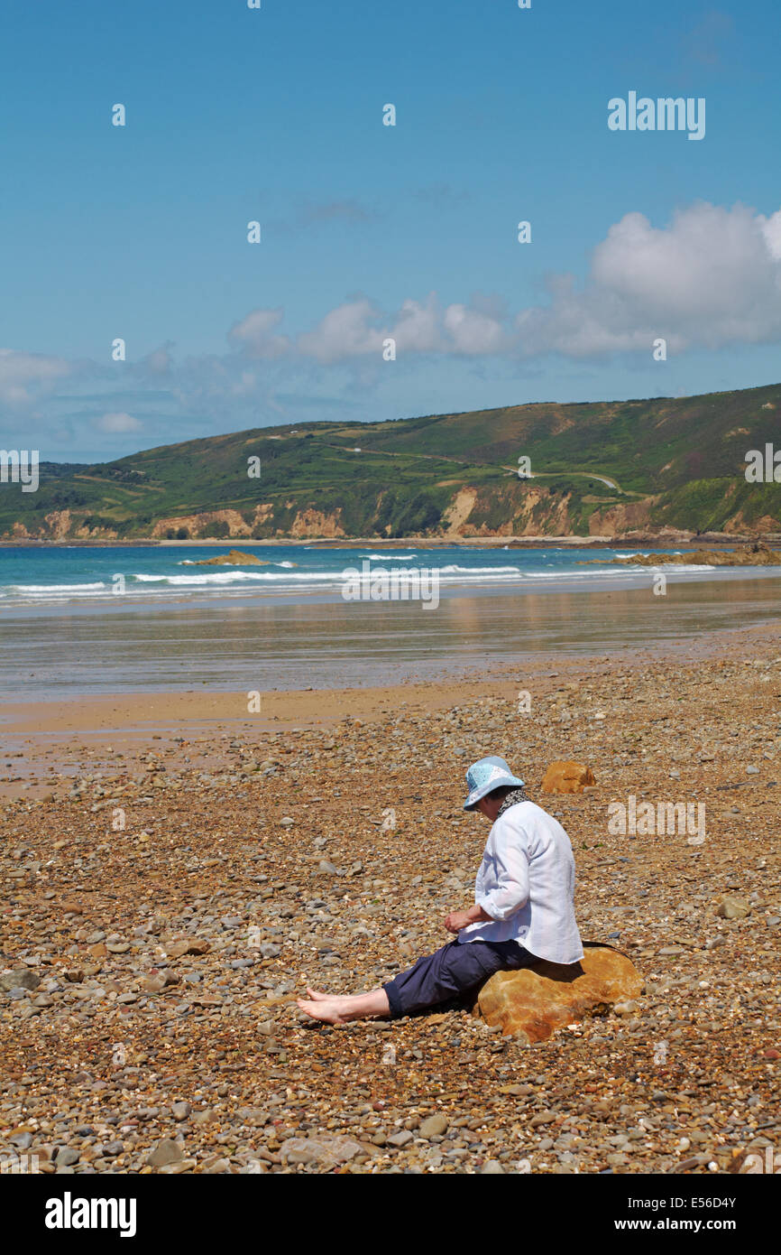 Frau sitzt auf Felsen am Strand von Vauville, Normandie, Frankreich im Juli Stockfoto