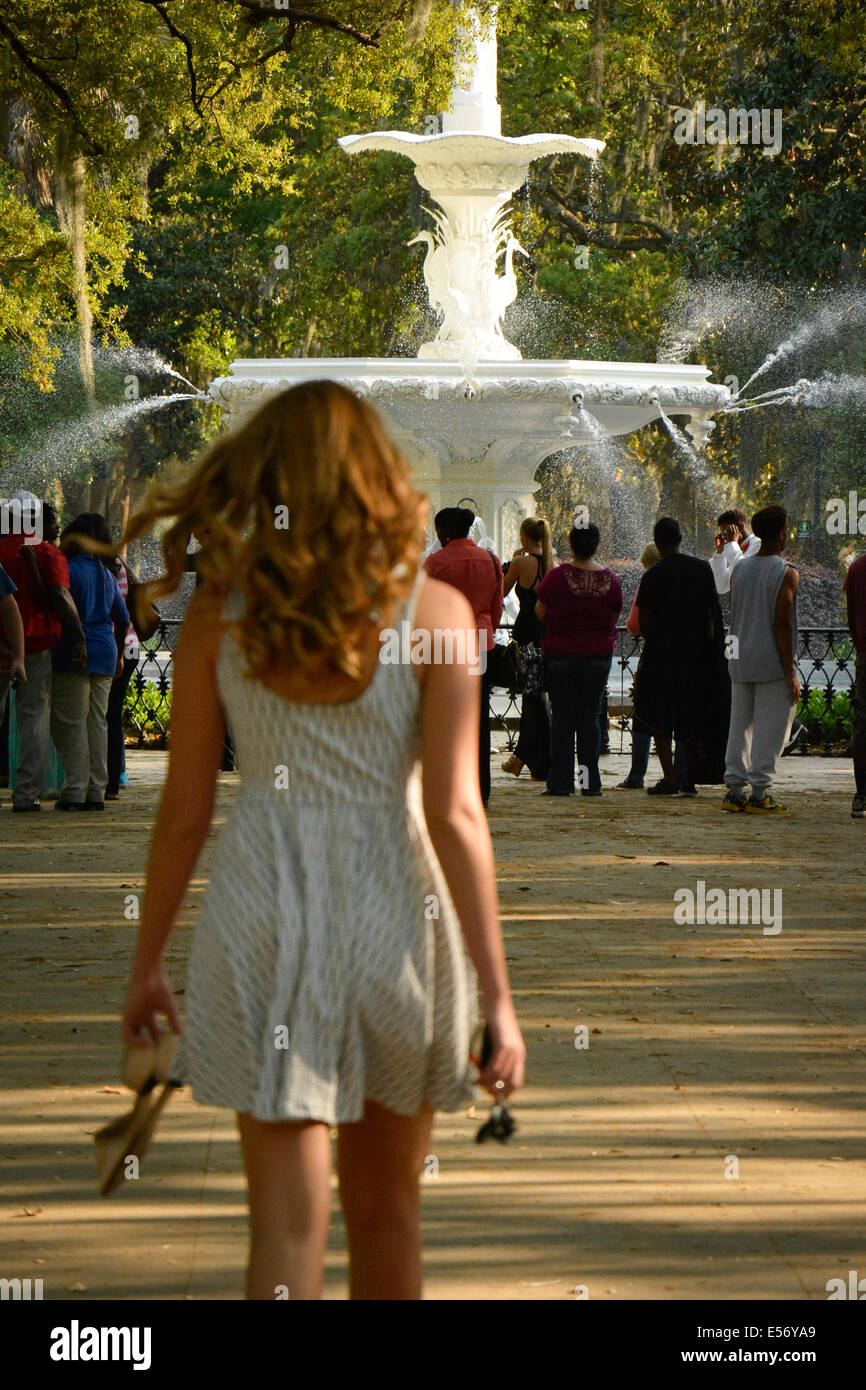 Rückansicht einer jungen weißen Frau mit langen Haaren in einem Sommerkleid, nähert sich die Menschenmenge in Forsyth Park nahe dem Brunnen, Savannah, GA Stockfoto