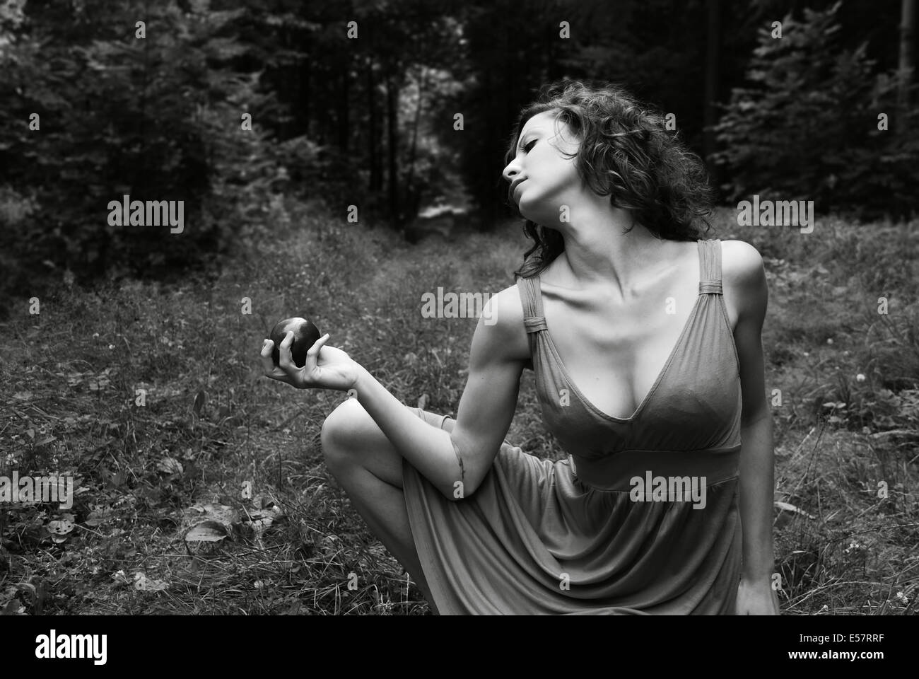 Eine Mädchen wirft draußen im Wald mit einem Apfel. Wie Eva im Garten Eden sitzt sie nachdenklich mit Blick auf den Apfel. Stockfoto