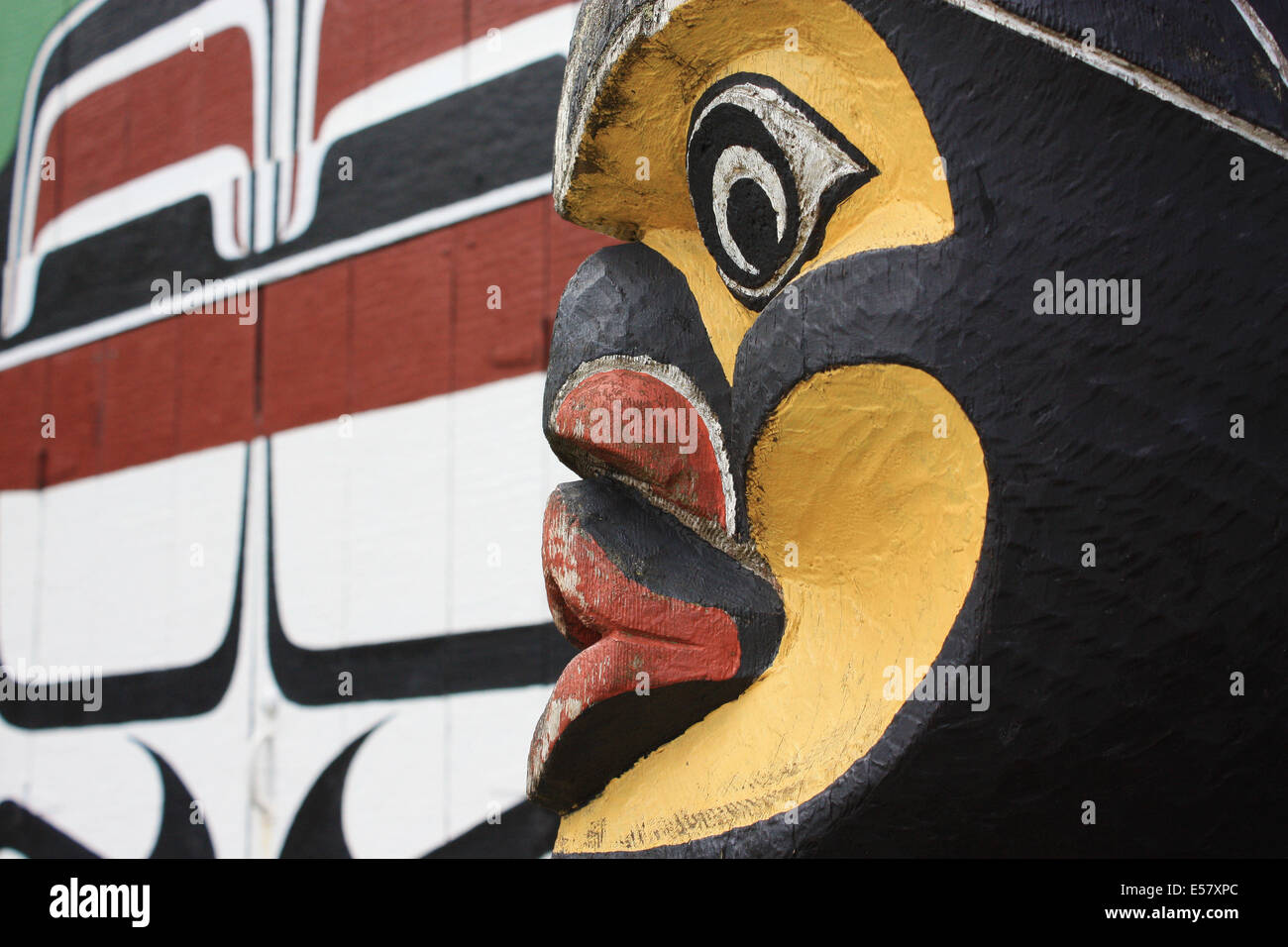Indianer Totempfahl Gesicht, eingefangen von Seite mit Langhaus Wand im Hintergrund (lackiert) Stockfoto
