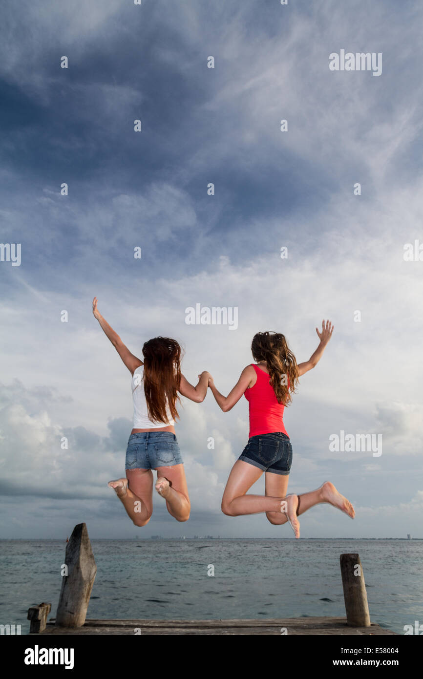 Zwei junge Mädchen springen in Glück in eine atemberaubende Seenlandschaft am pier Stockfoto