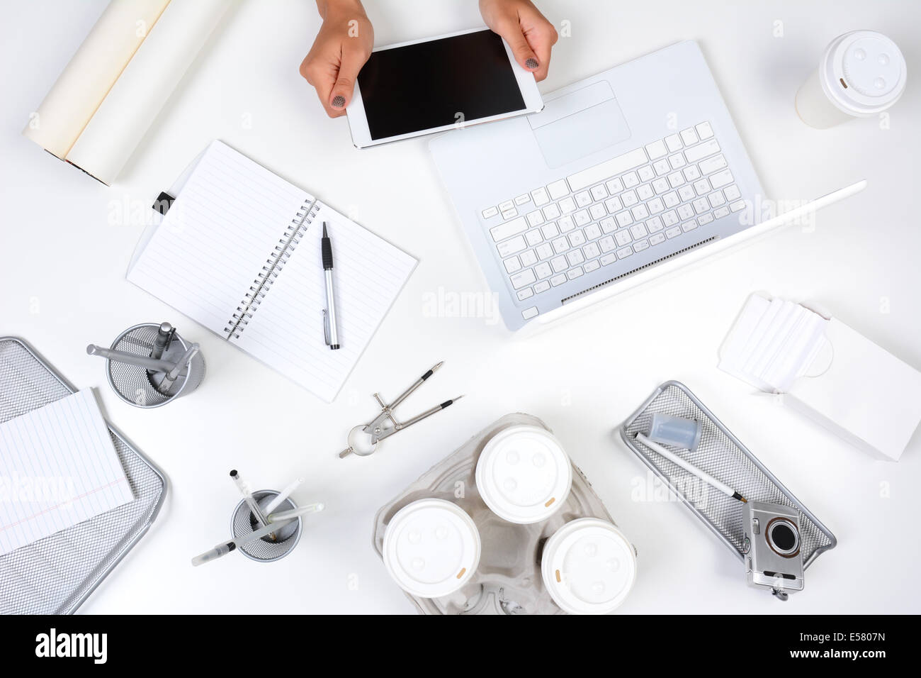 Hohen Winkel geschossen aus einem weißen Schreibtisch mit vorwiegend weißer und silberner Office-Objekte, mit einer Frau mit einem Tablet-Computer zeigt h Stockfoto