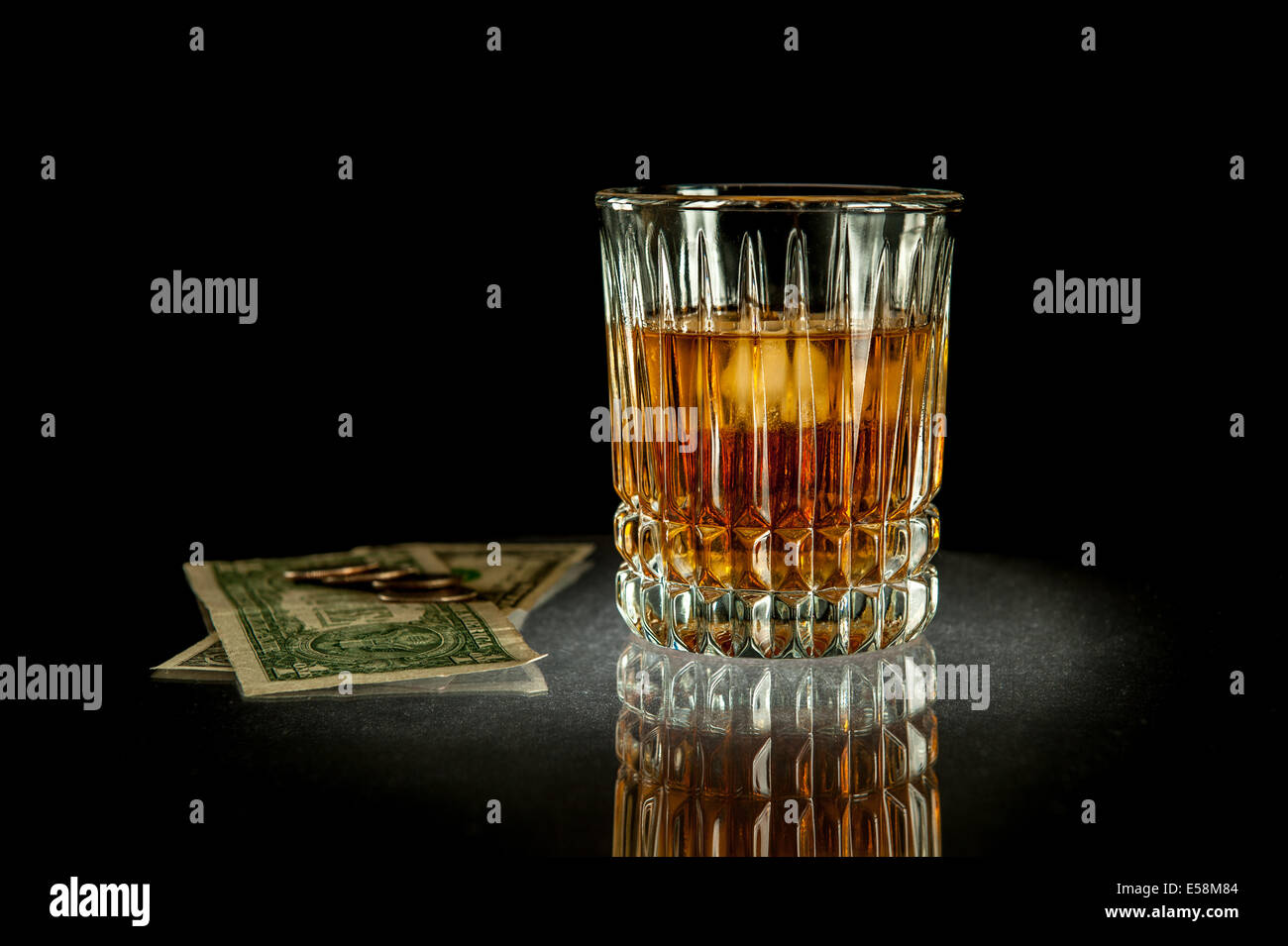 Foto von einem Glas Whiskey neben Dollarnoten und Viertel-Dollar-Münzen. Stockfoto
