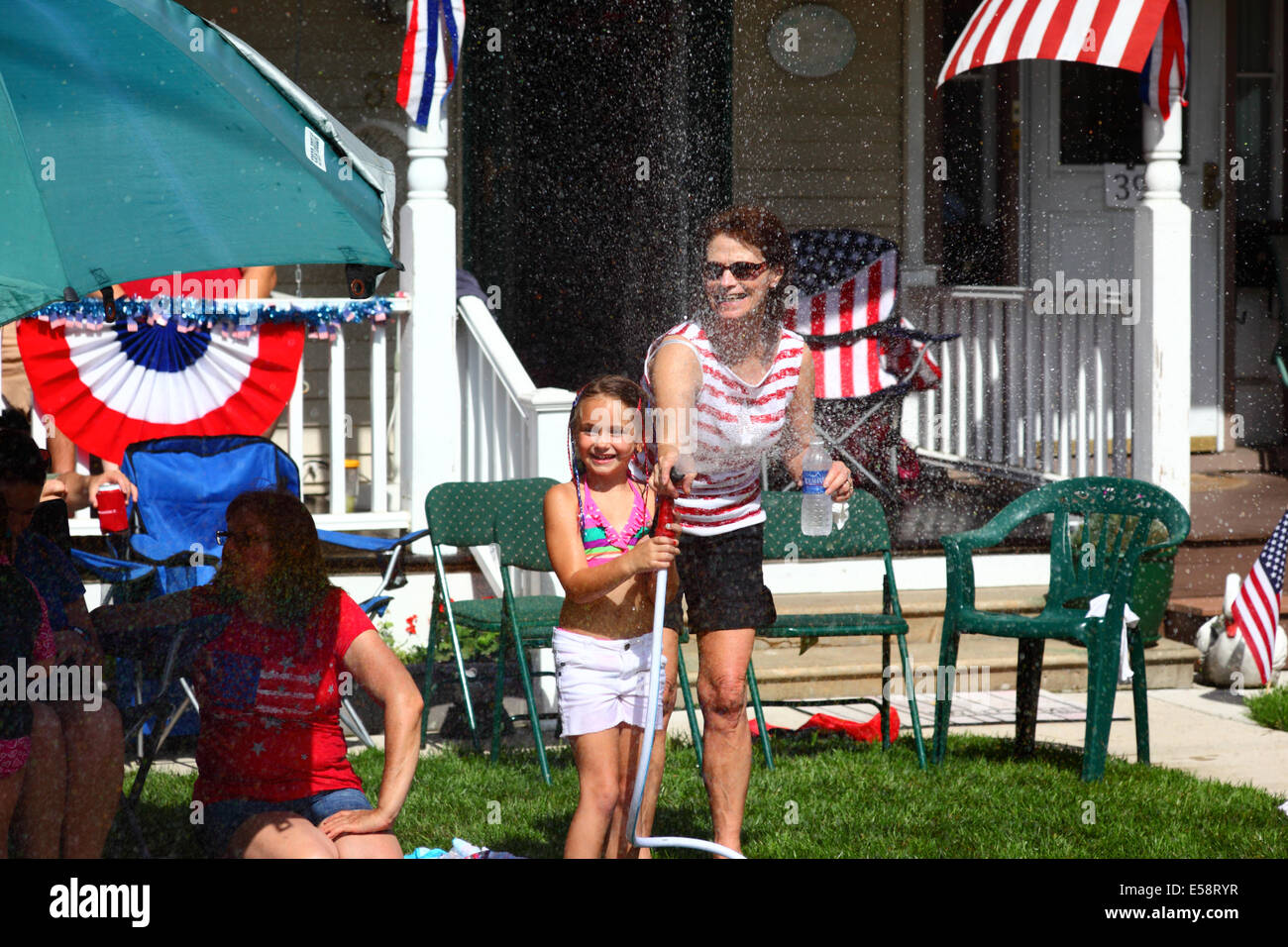 Mädchen und ihre Mutter, die am 4th. Juli an einem Feiertag des Unabhängigkeitstages in Catonsville, Maryland, USA, vor der Veranda mit einer Schlauchleitung spielen Stockfoto