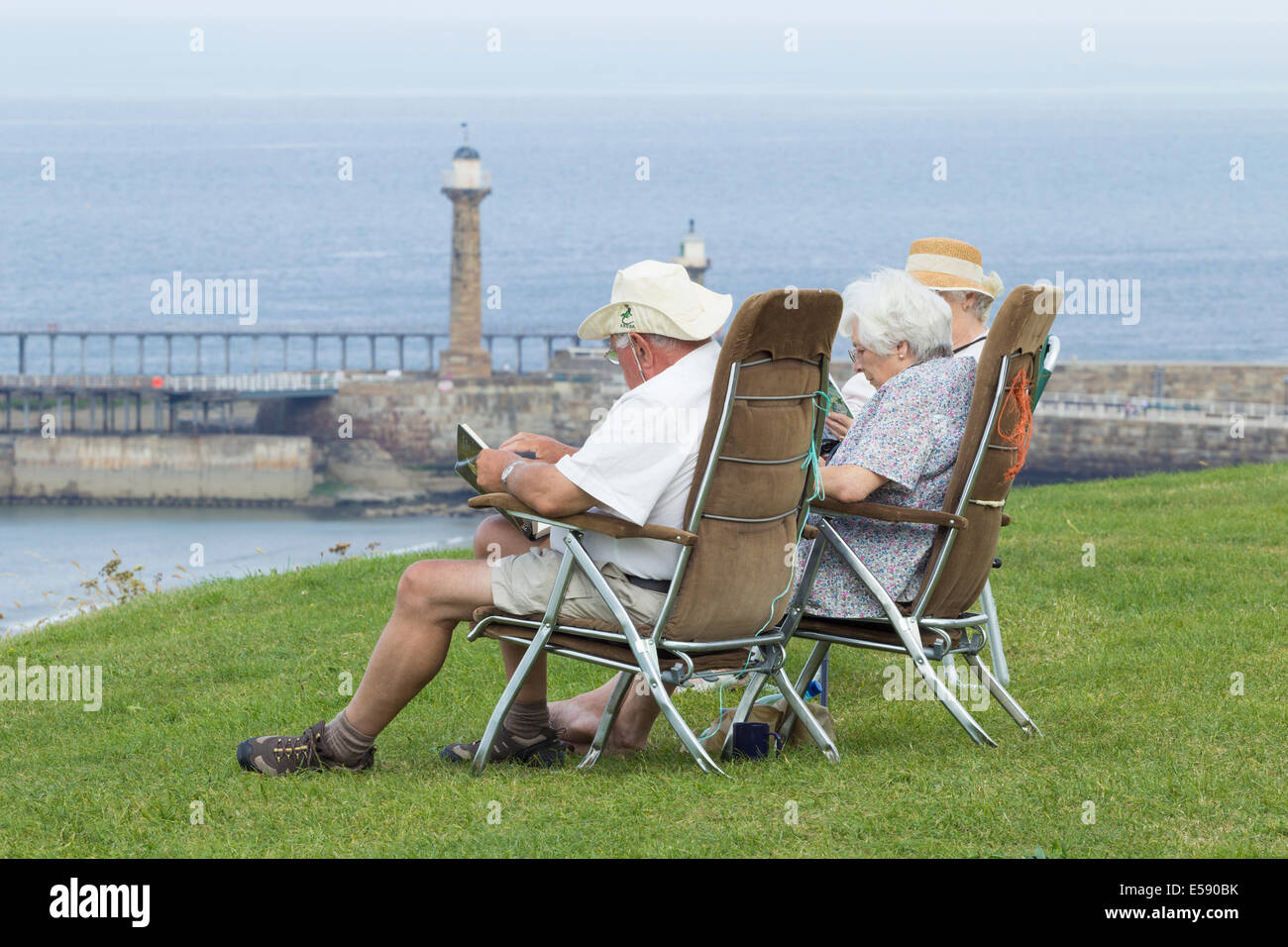 Ältere Menschen lesen und genießen das warme Wetter bei Whitby, North Yorkshire, England, UK Stockfoto