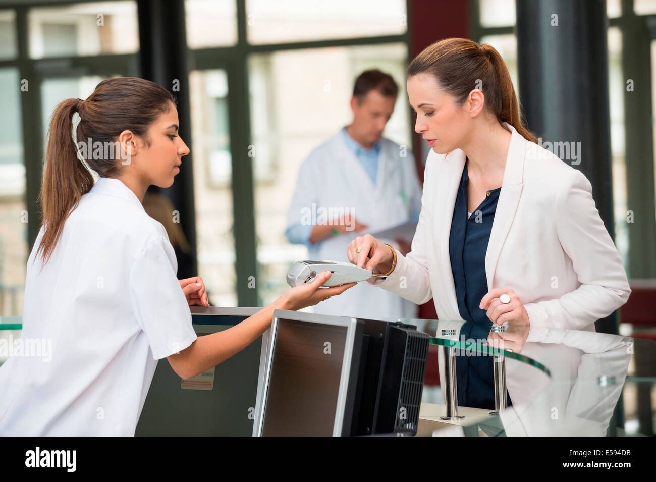 Ärztin, die die Zahlung mit Kreditkarte an Krankenhaus-Rezeption Stockfoto