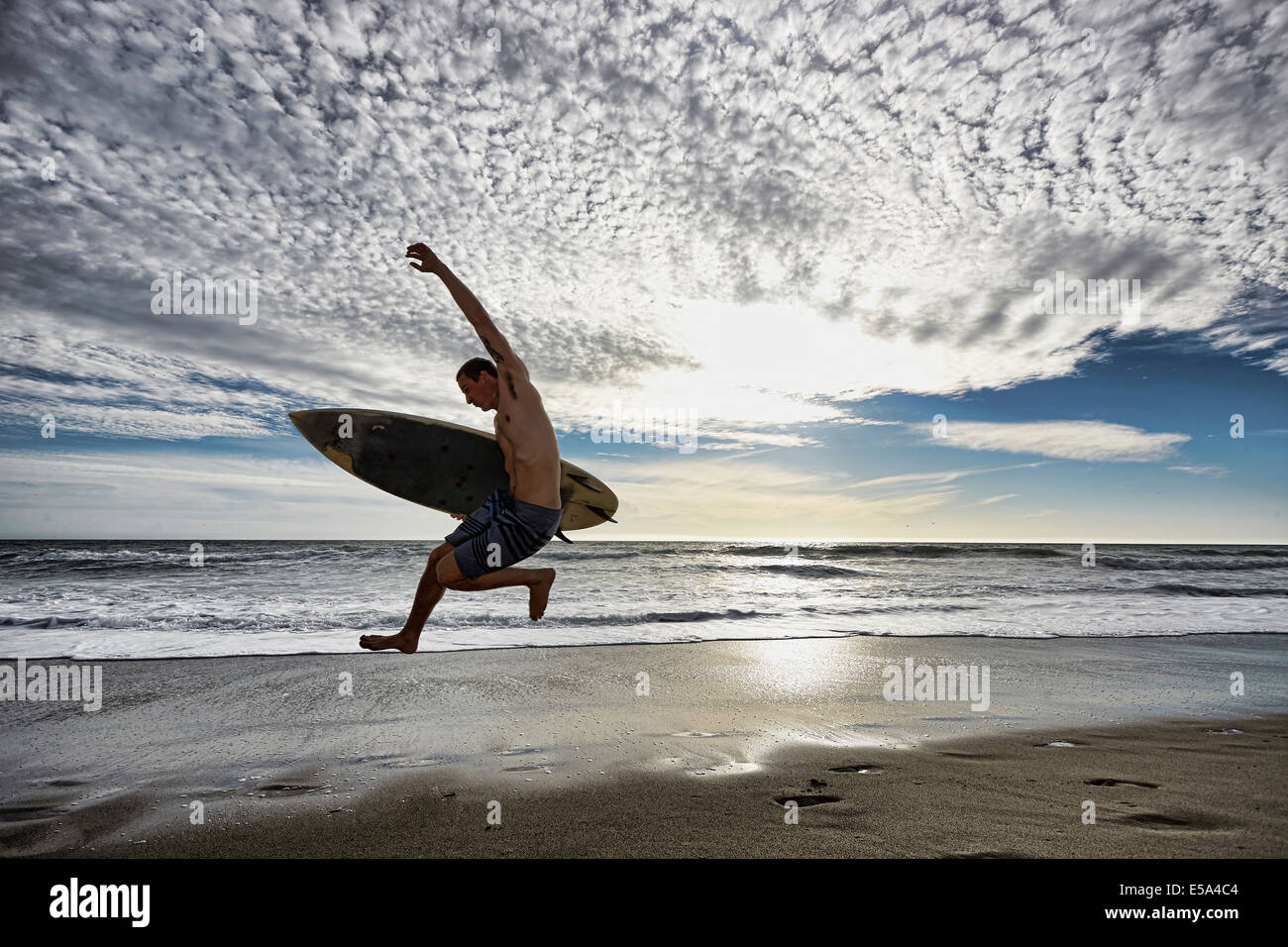 Kaukasischen Mann springt mit Surfbrett am Strand Stockfoto