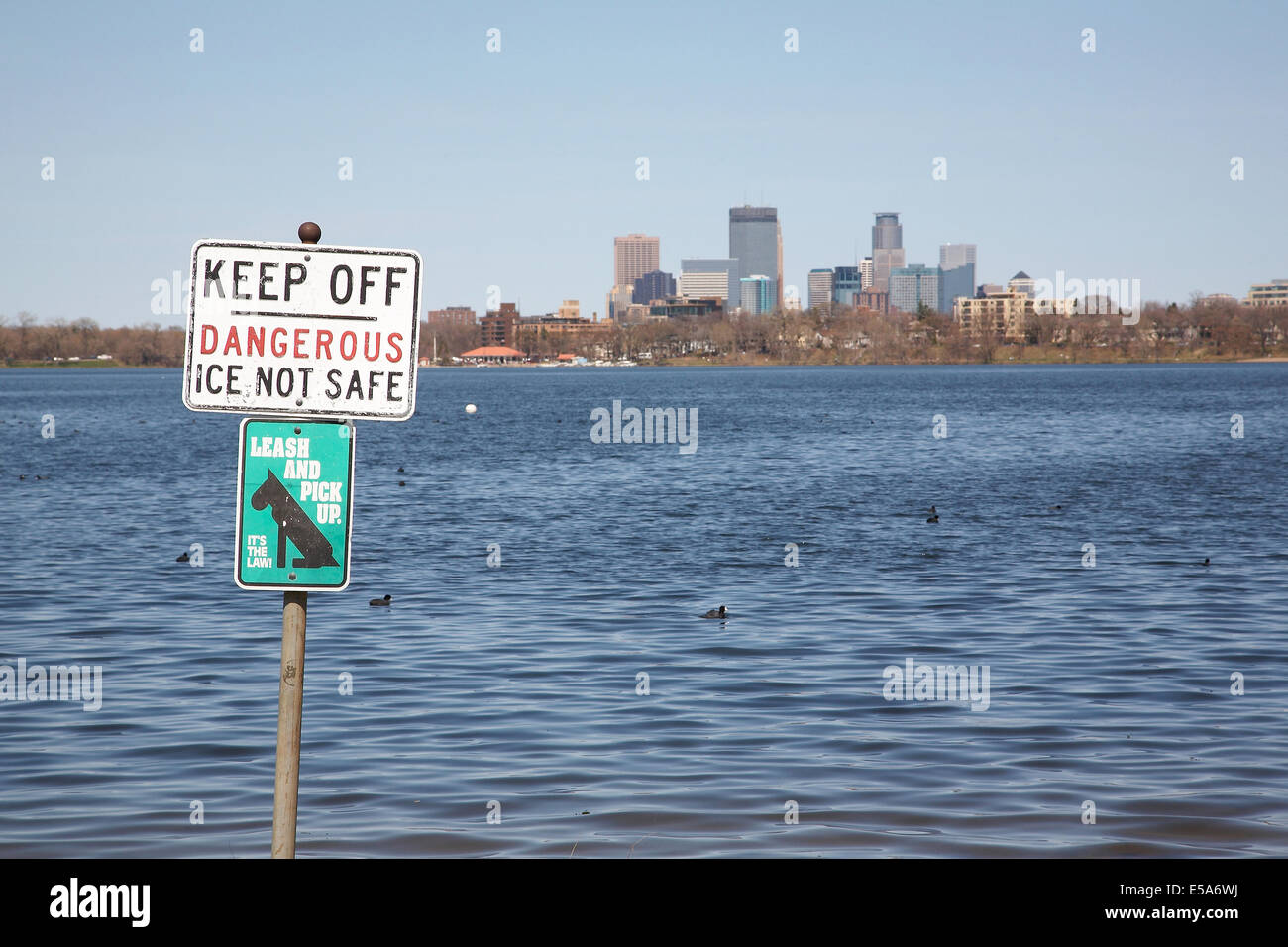 Ein Warnschild am Ufer des Lake Calhoun mit der Stadt von Minneapolis in der Ferne. Stockfoto