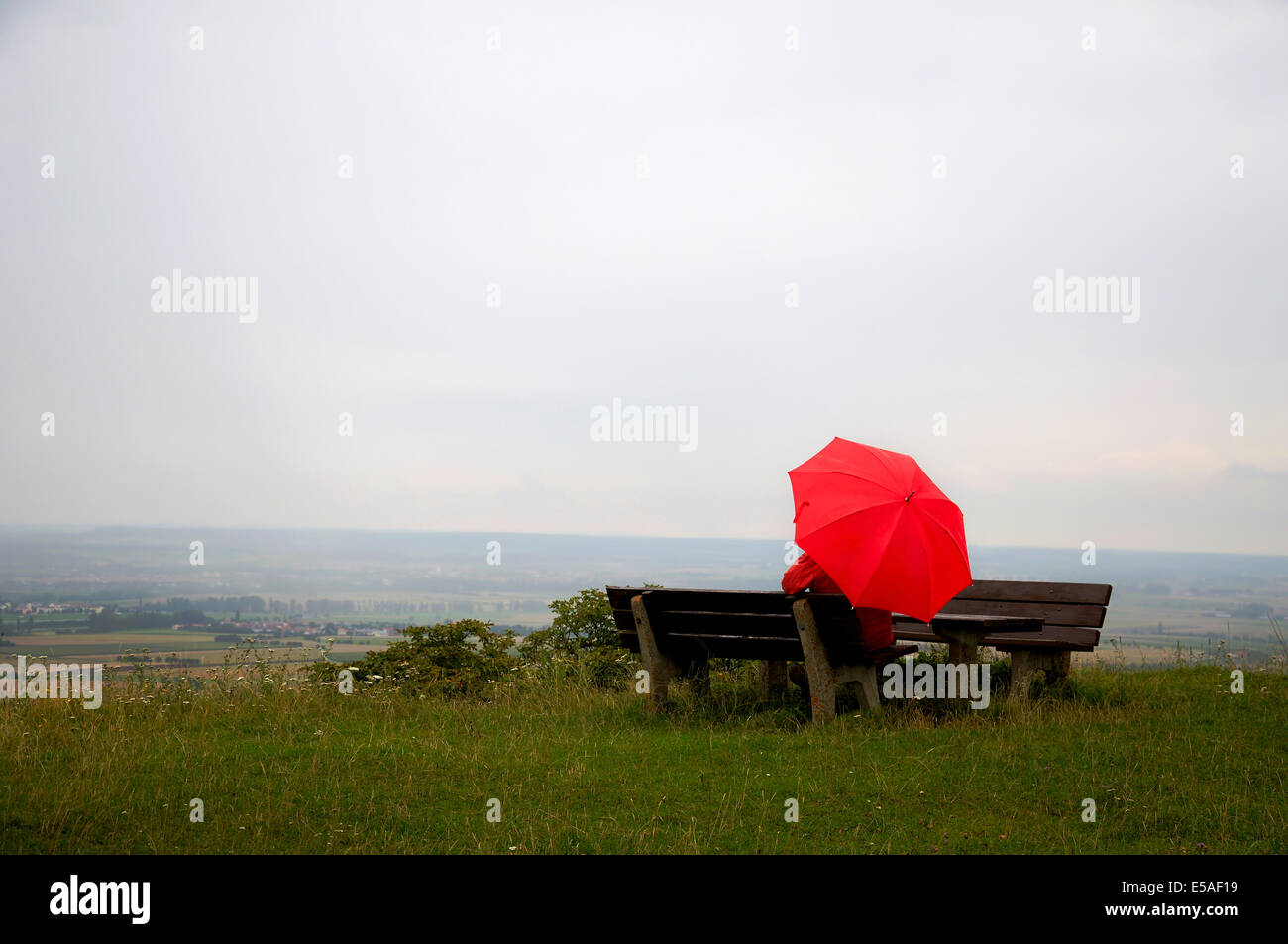 Mann mit rotem Schirm sitzen auf einer Bank an einem regnerischen Tag Stockfoto