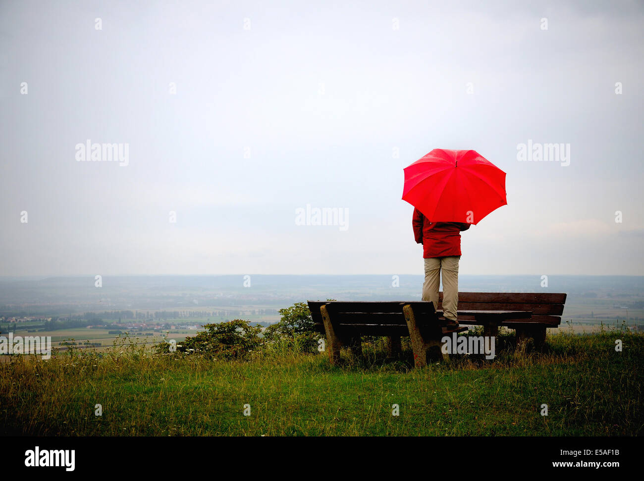 Mann mit roten Regenschirm stehen auf einem Aussichtspunkt an einem regnerischen Tag Stockfoto