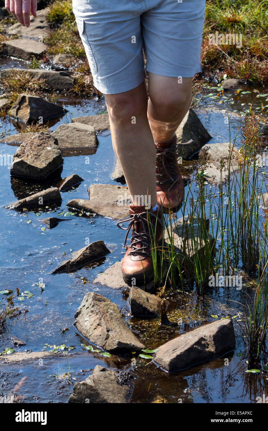 Eine Frau Wanderer mit Stepping Stones um zu überqueren Sie einen Stream bei The Grey Man Weg Fair Kopf Co Antrim N Ireland Stockfoto