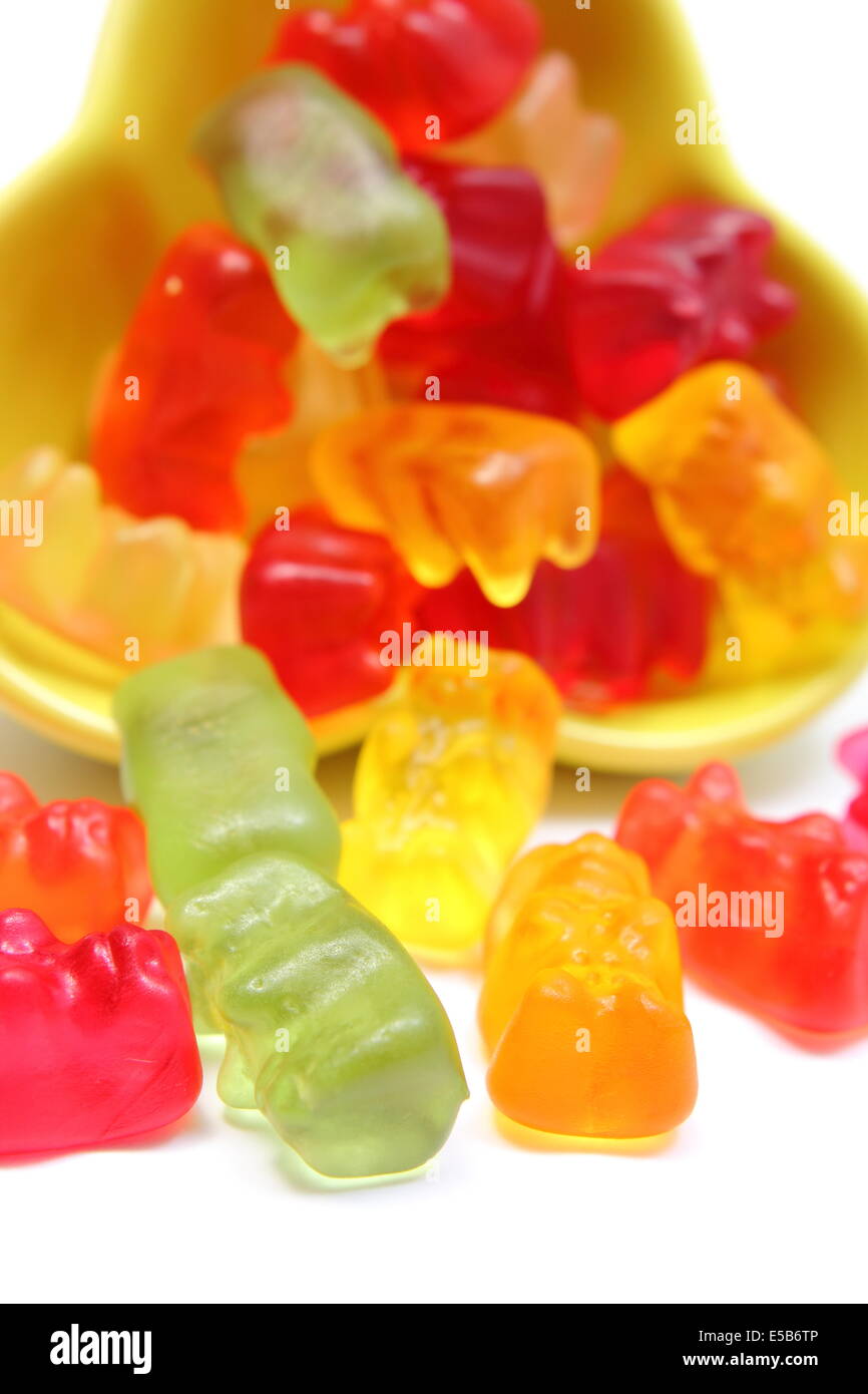 Nahaufnahme von vielen bunten Haribo Bären Bonbons aus gelben Schale gießen. Isoliert auf weißem Hintergrund Stockfoto