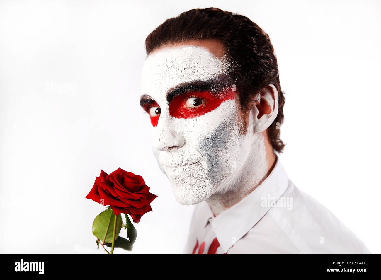 Mann mit weißen Mascara und blutigen Shirt hält rote rose Stockfoto