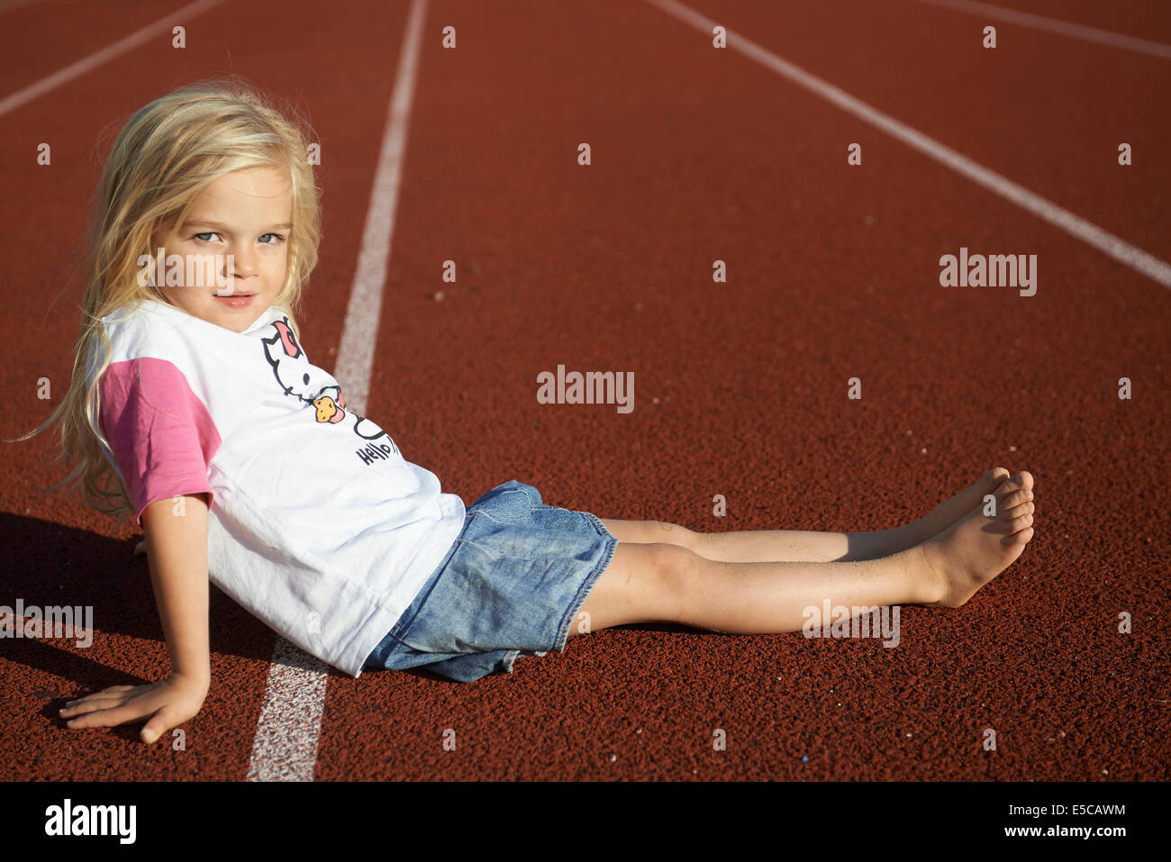 Kind etwas blondes Mädchen sitzen auf Tartan Laufstrecke im Stadion Stockfoto