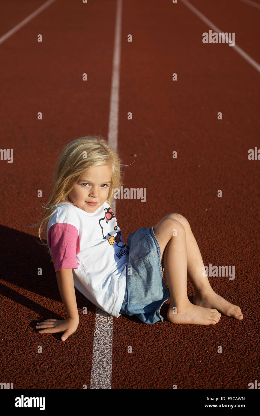 Kind etwas blondes Mädchen sitzen auf Tartan Laufstrecke im Stadion Stockfoto