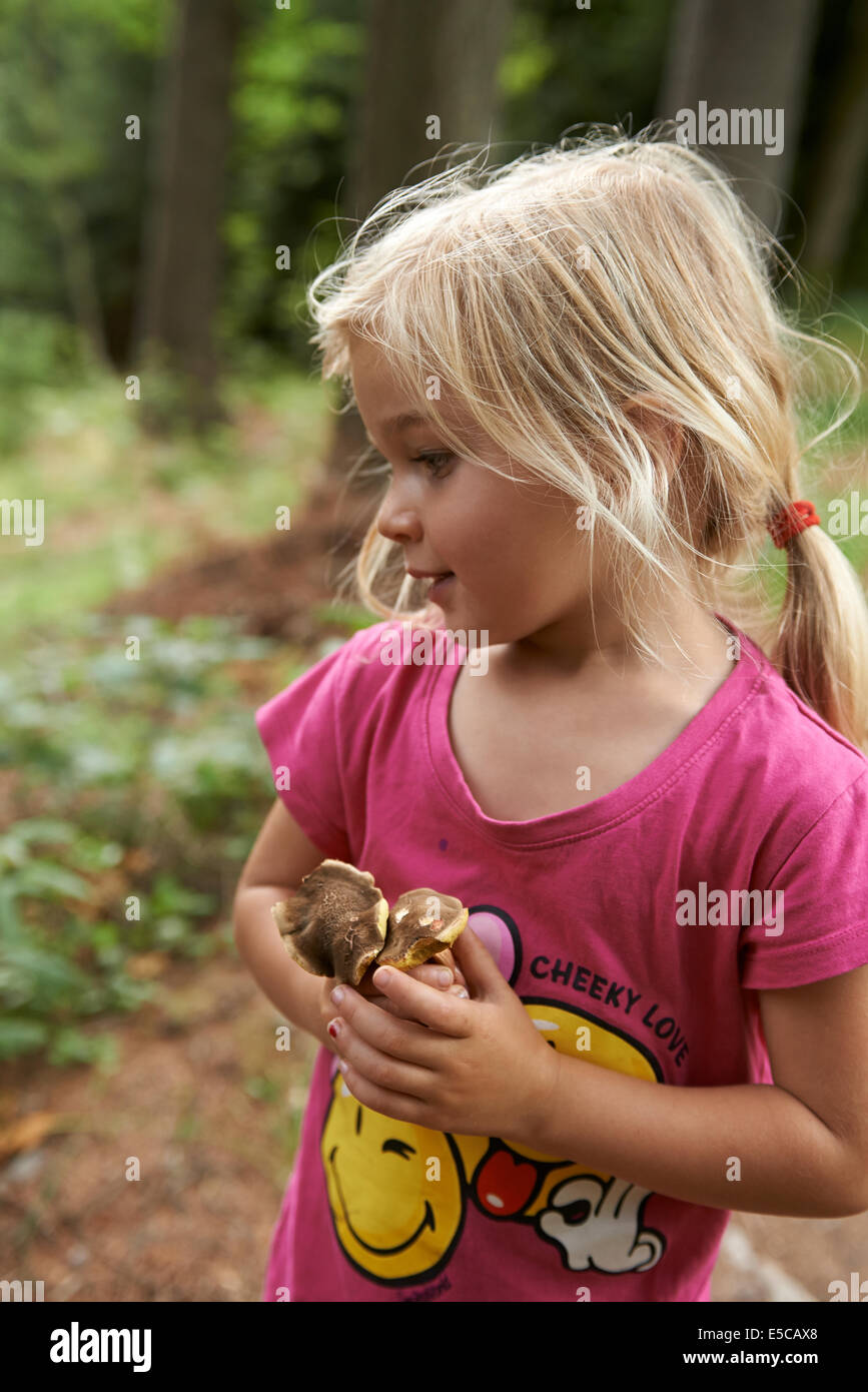 Porträt von glückliches Kind blondes Mädchen, Kommissionierung und Transport volle Händen der Pilze draußen im Wald Stockfoto