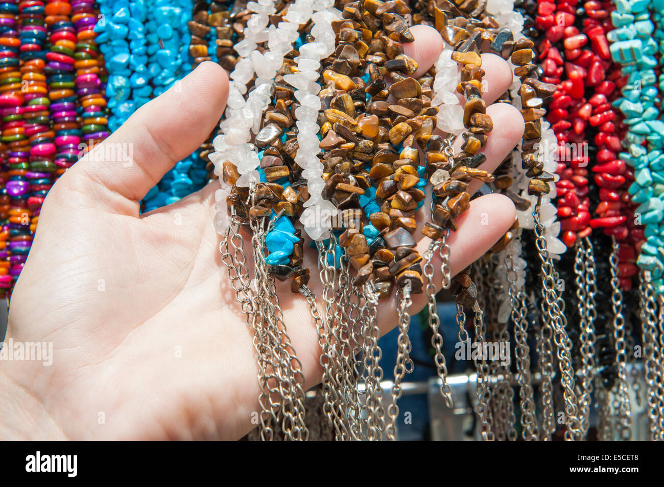 Shopper-Hand mit reich verzierten farbigen Stein Schmuck hängen in Reihe am Marktstand Stockfoto