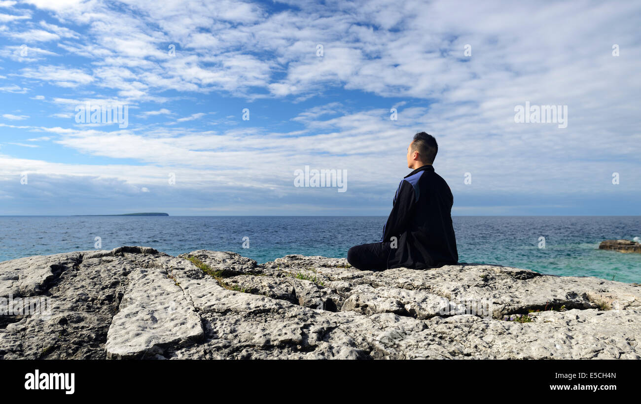 Meditierenden sitzt auf einem Felsen am Ufer eines Sees. Bruce Peninsula, Ontario, Kanada. Stockfoto