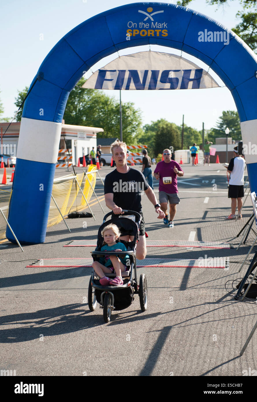 Mann in 5K oder 10K Marathon Rennen Kreuzung Ziellinie mit Baby im Kinderwagen Stockfoto