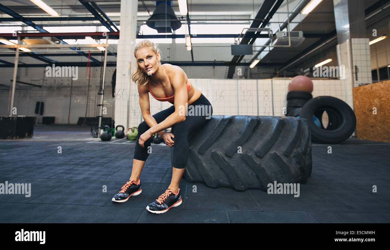 Schöne und starke junge Frau sitzt auf einem großen Reifen nach ihrer Übung. Frau Pause nach Crossfit Training im Fitness-Studio. Stockfoto