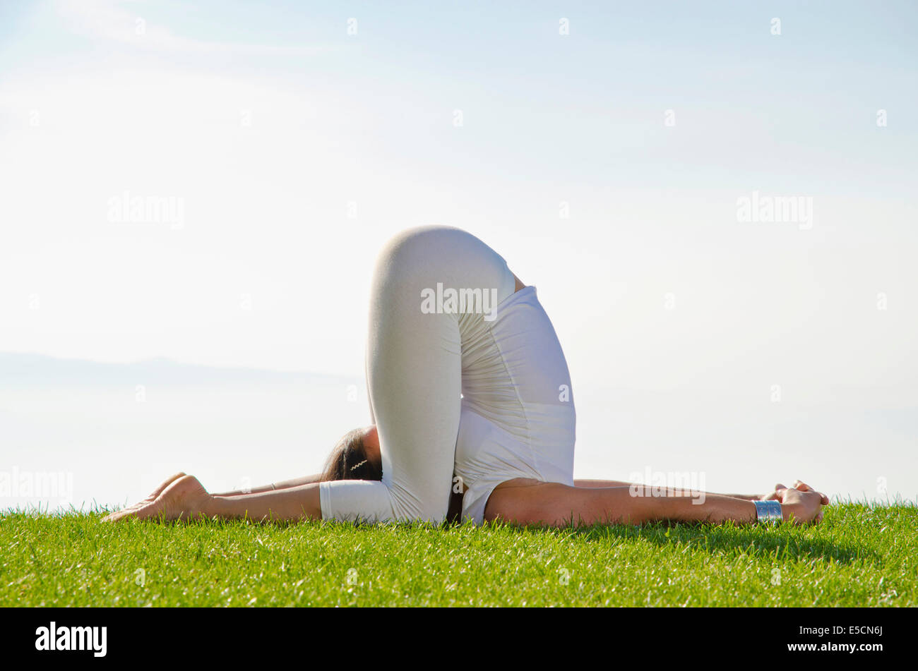 Junge Frau praktizieren Hatha-Yoga, hier eine Variation der Variation des Pfluges, Halasana, karnapidasana Stockfoto
