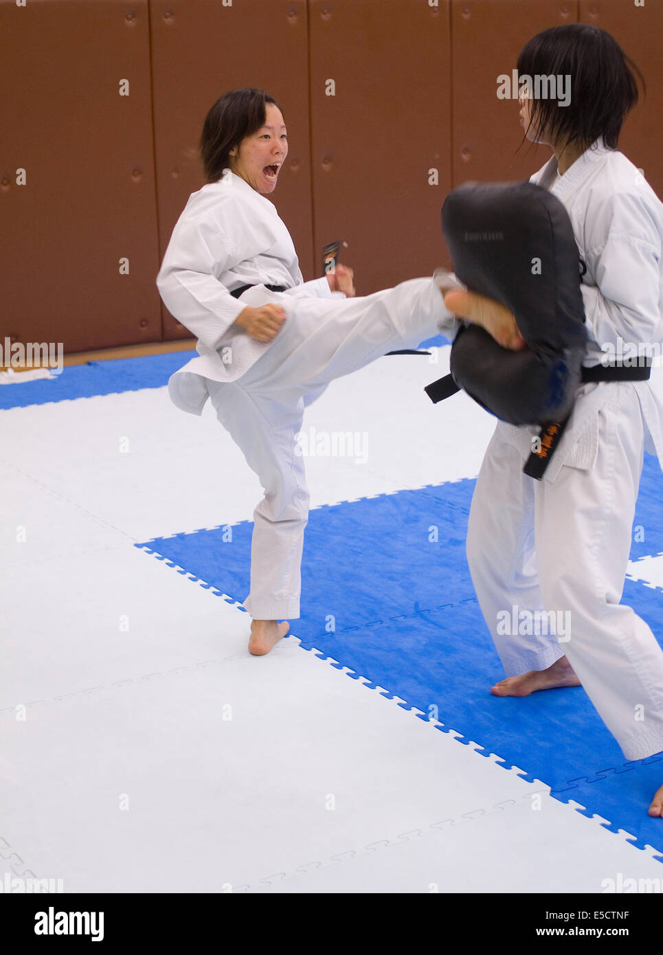Japanische Jugendliche üben Karate Tritte gegen Auflagen. Stockfoto