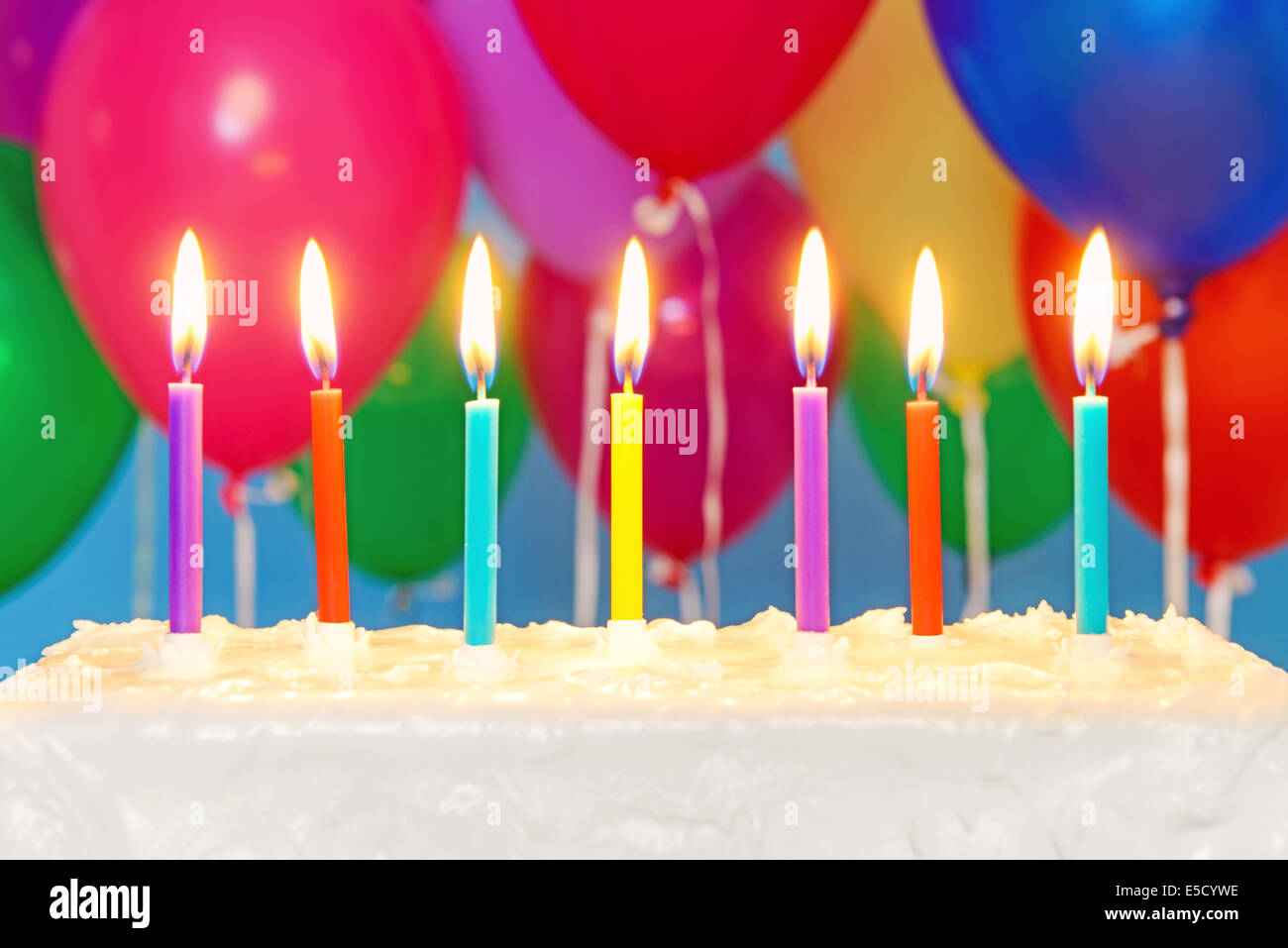 Kerzen brennen auf eine weiße iced Geburtstagstorte mit bunten Luftballons im Hintergrund, Textfreiraum auf dem Kuchen, fügen Sie Ihre Stockfoto