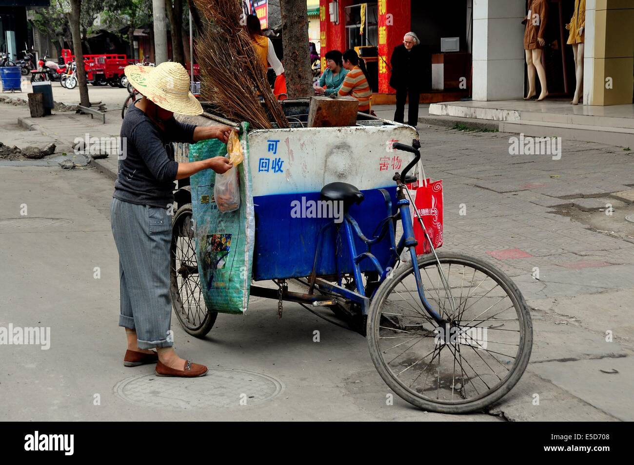 JIU-CHI-TOWN (SICHUAN), CHINA: Street-Putzfrau trägt einen Strohhut mit ihrem Fahrrad Warenkorb und Besen altmodisch aus Zweigen Stockfoto