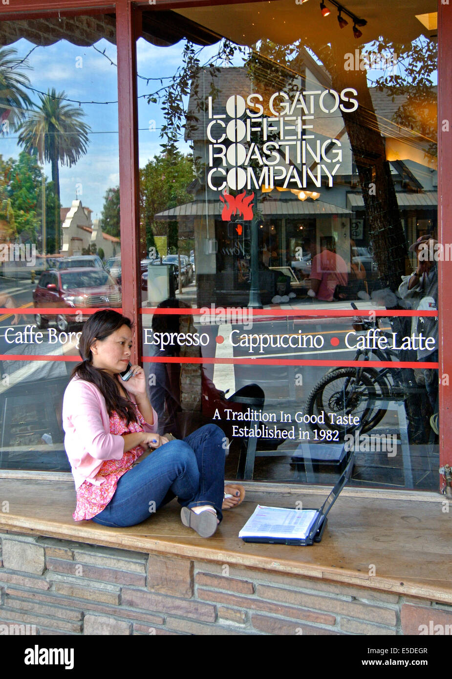 Frau am Telefon plaudert und funktioniert auf Laptop sitzend auf Bank Coffee-shop Stockfoto