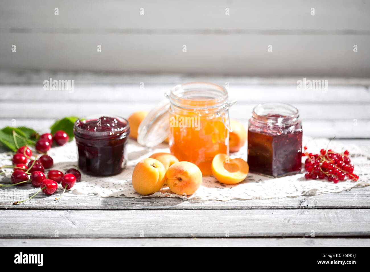 Kirschmarmelade und Kirschen, Marillenmarmelade und Aprikosen, Johannisbeeren Marmelade und rote Johannisbeeren auf dolly Stockfoto