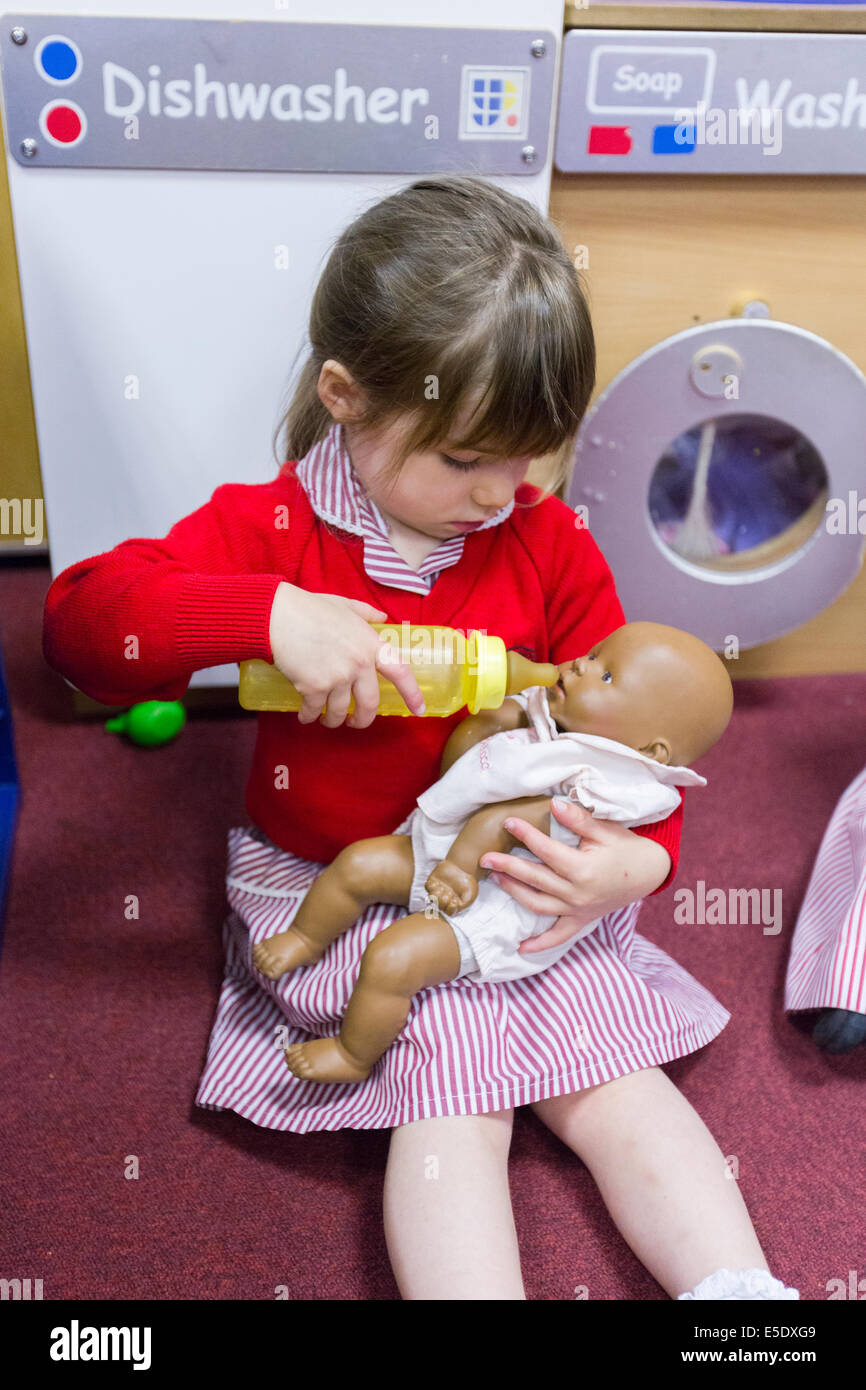 Ein Mädchen in einer UK-Grundschule, die vorgibt, eine Babypuppe mit einer Flasche füttern Stockfoto