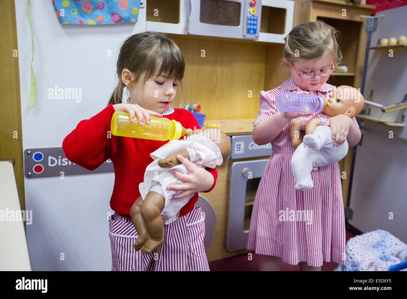 Zwei Mädchen an einer britischen Grundschule vorgibt, baby Puppen mit einer Flasche zu füttern Stockfoto