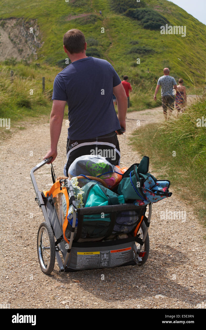 Man zieht Rahmen voller Strand Artikel gehen hinunter zum Strand bei Worbarrow Bay, Isle of Purbeck, Dorset im Juli Stockfoto